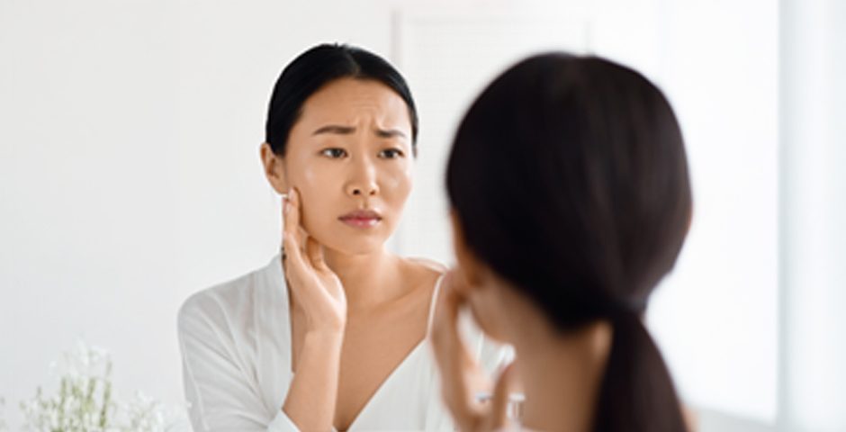 鏡を見ながらシミや肌トラブルに悩む女性