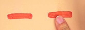 人工皮膚に塗布した2本の帯のうち、右側の帯を人さし指の腹で押さえてこすっている。帯の表面が指でなぞられ、縁がわずかに乱れている
